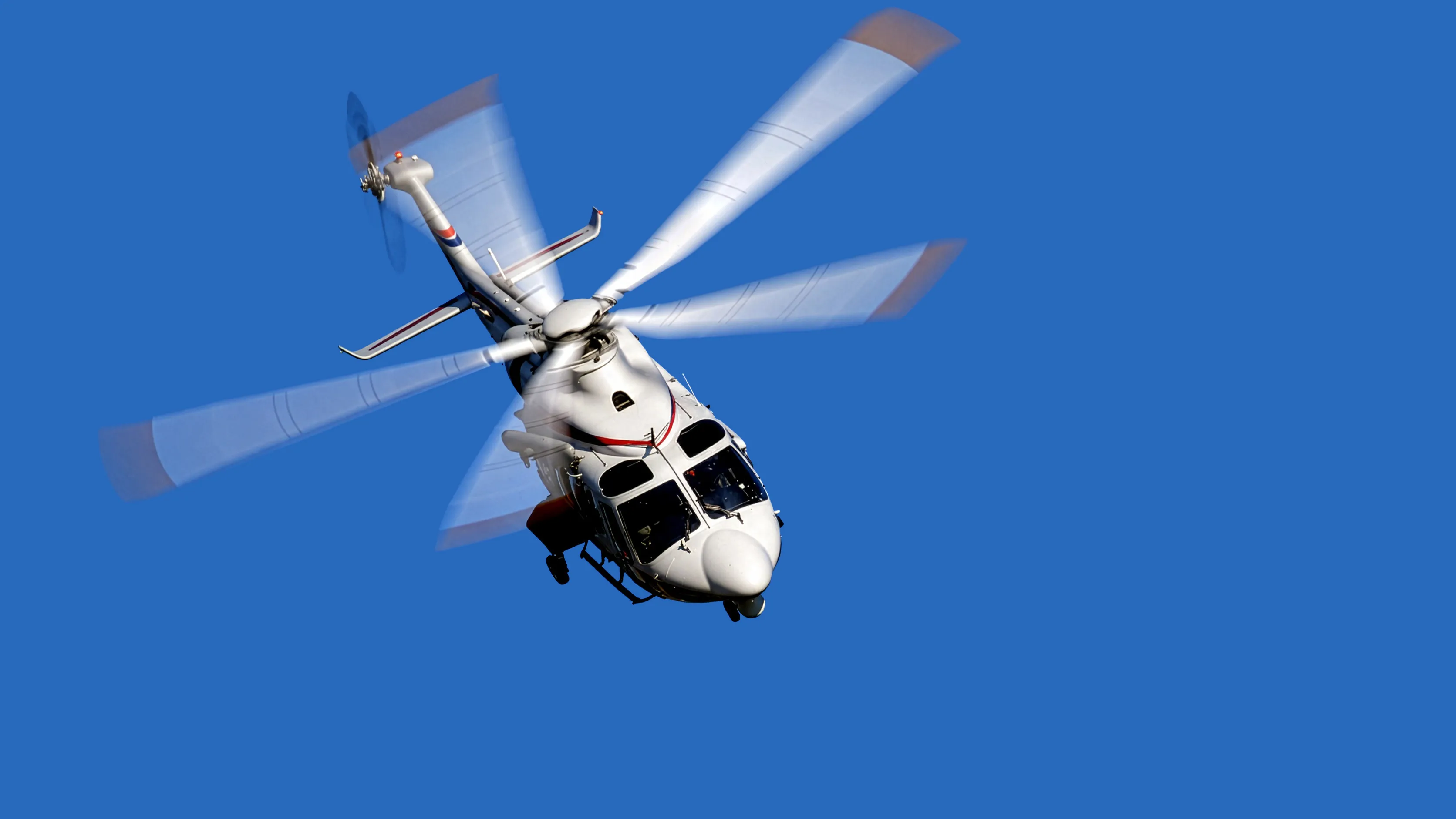A medium twin-engine executive helicopter in cruise flight against open sky, the kind of short between-stops leg that links a roadshow day together.