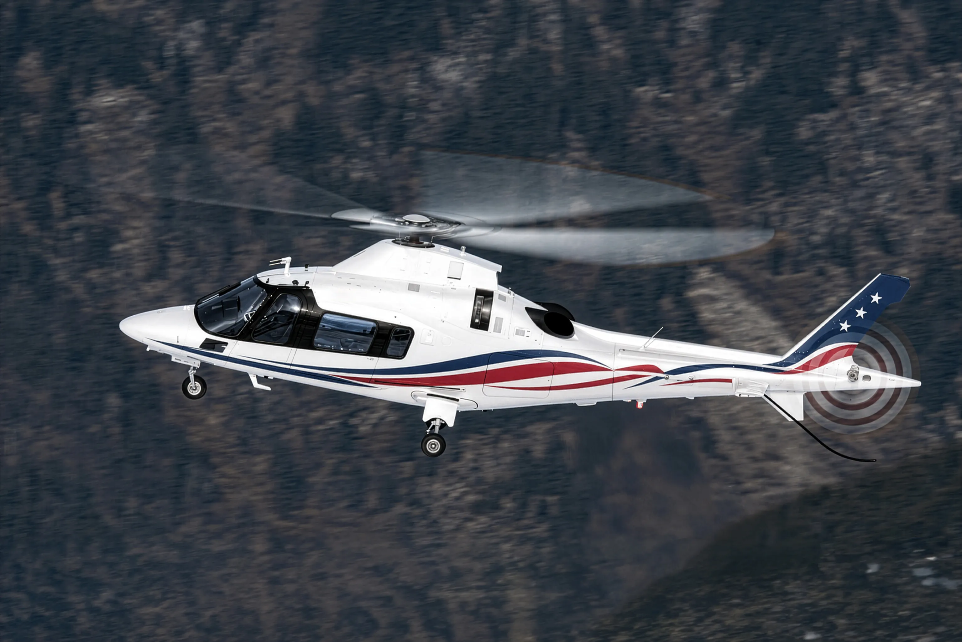 A white light twin-engine helicopter with red and blue striping in flight past forested mountain slopes, the class used when a golf group outgrows a light single.