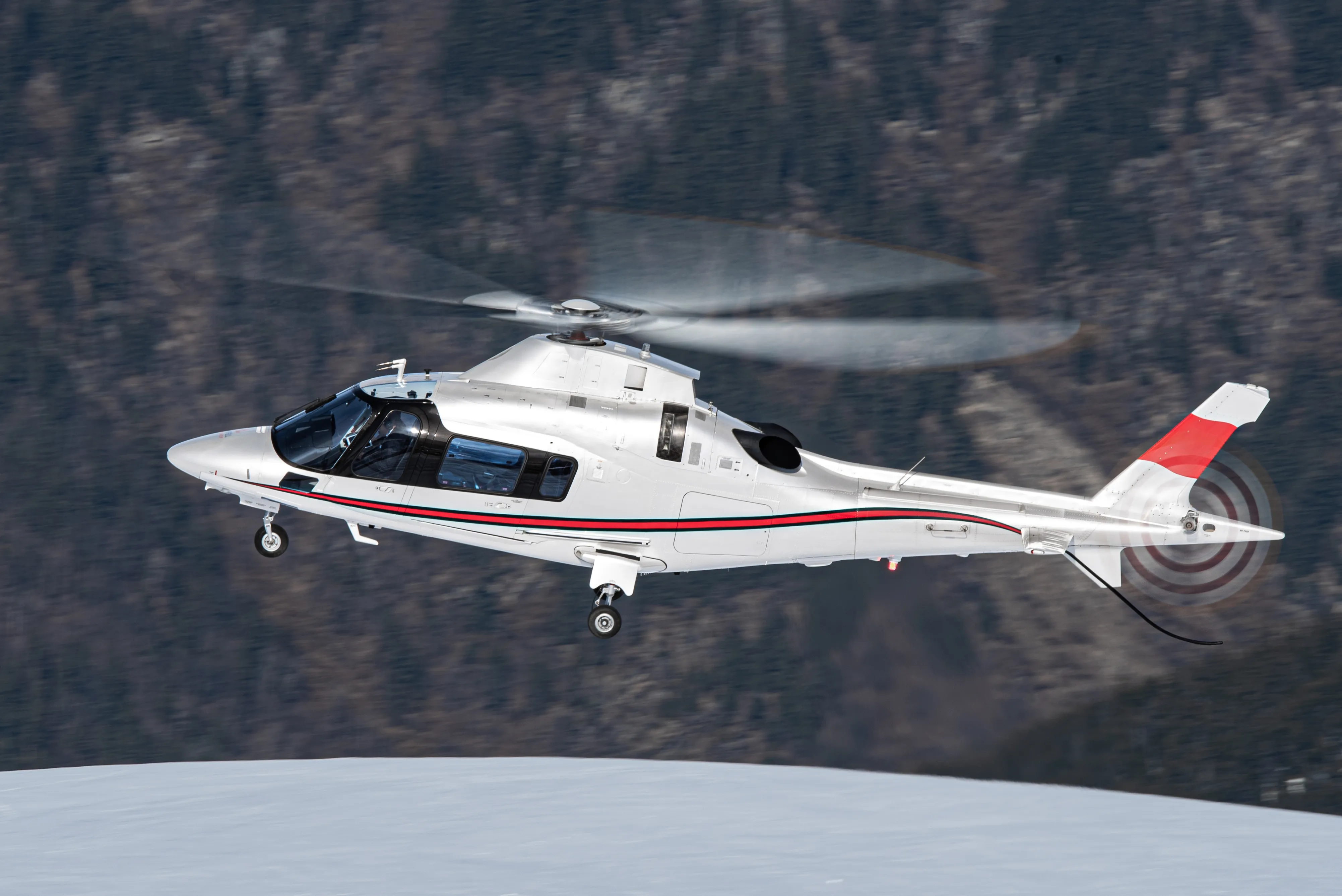 A white twin-engine helicopter in flight past a snow-dusted mountain ridge, the class used when a weekend trip outgrows a light single.