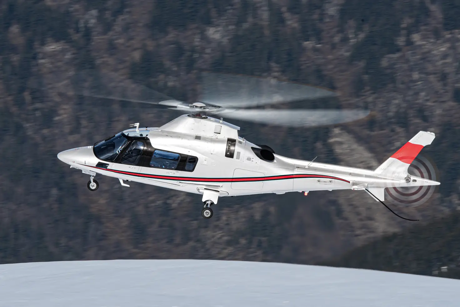 A white twin-engine helicopter in flight past a snow-dusted mountain ridge, the class used when a weekend trip outgrows a light single.
